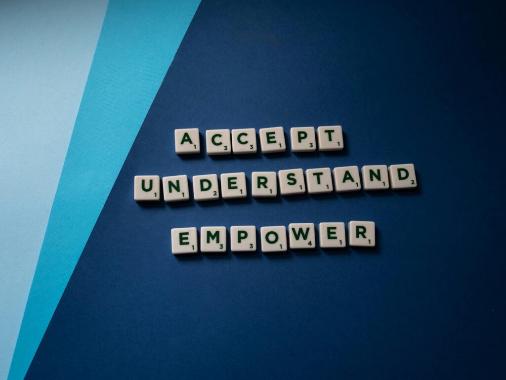 Scrabble letter tiles spelling 'Accept Understand Empower' on a blue background. Motivational and conceptual art.